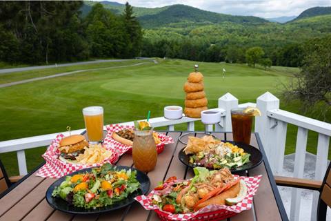 multiple plates of food with drinks on deck with golf course view