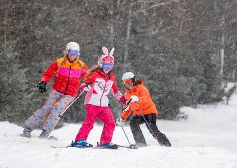 skier with bunny ears followed by two other skiers in colorful jackets
